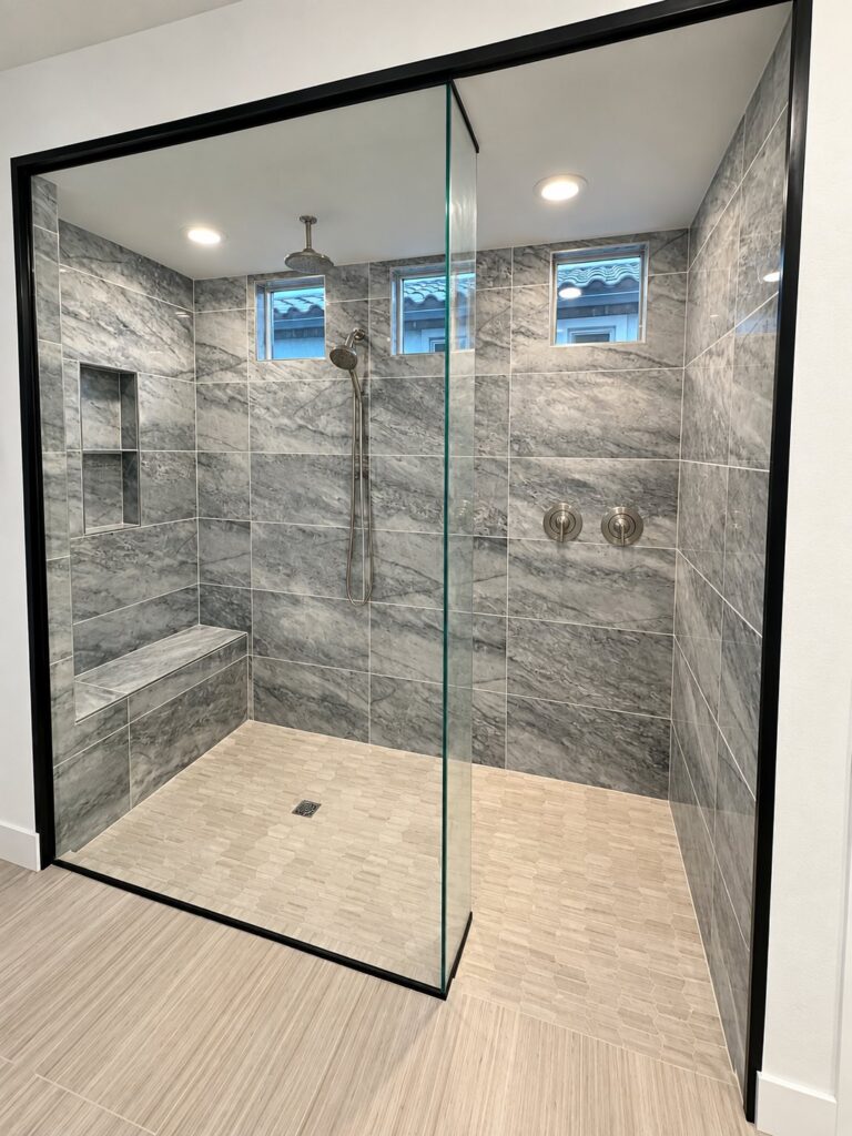 Large walk-in shower in gray stone-look tile with a bench, niche and black-framed glass