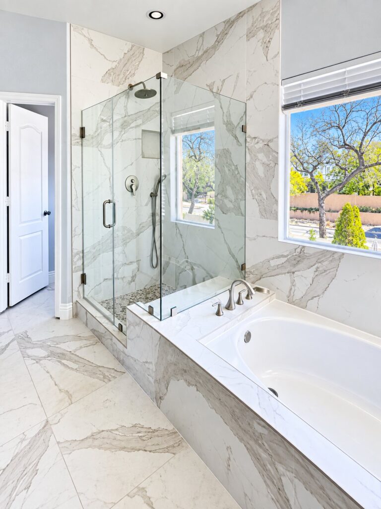 Glass shower beside a marble-look tub deck and large-format floor tile