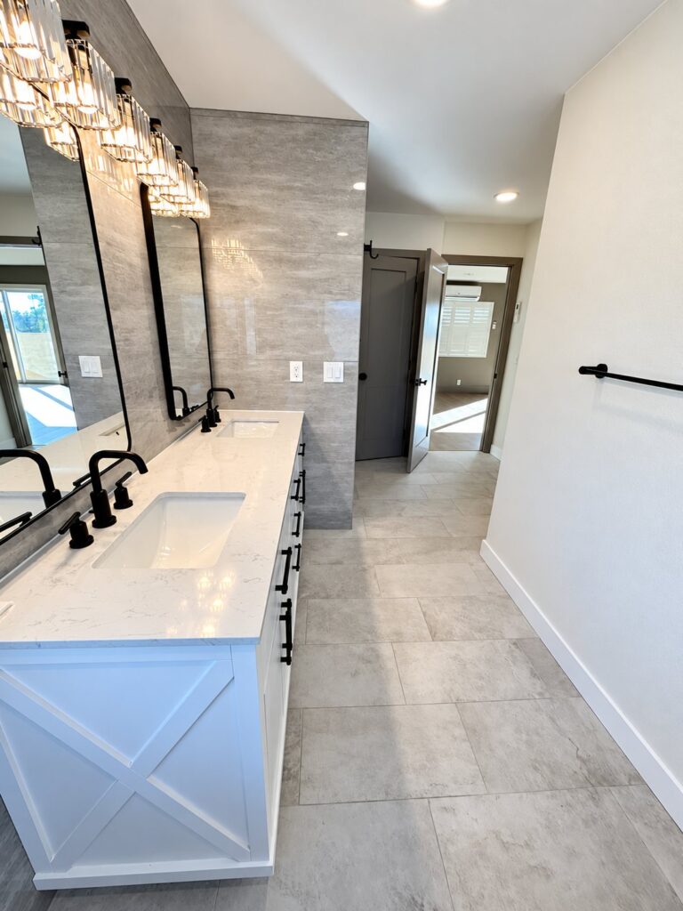 Long white double vanity with black fixtures and a crystal vanity light
