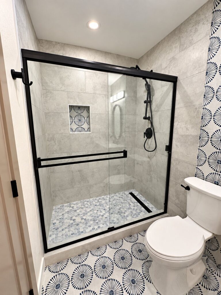 Tiled shower with a patterned niche, black sliding door and pinwheel floor tile