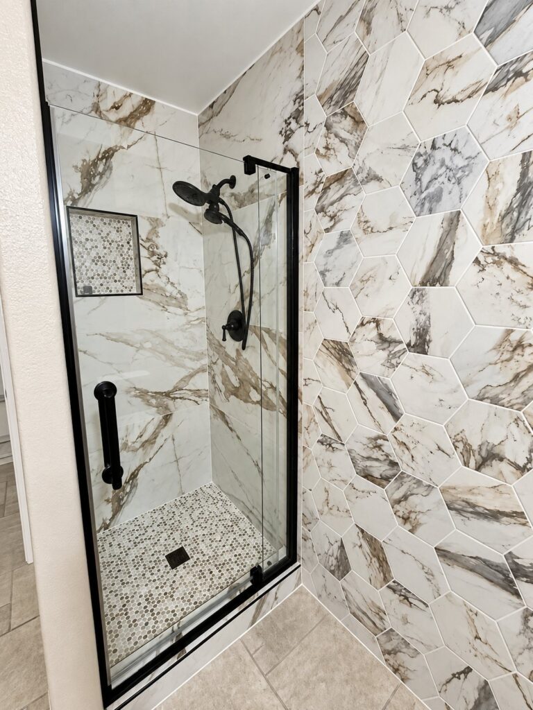 Shower in large hexagon marble-look tile with a mosaic niche and black glass door