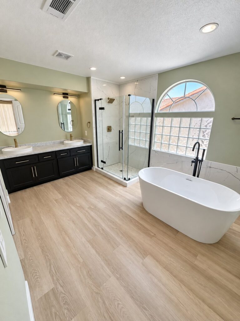 Bathroom with a freestanding tub, black double vanity and glass shower under an arched window