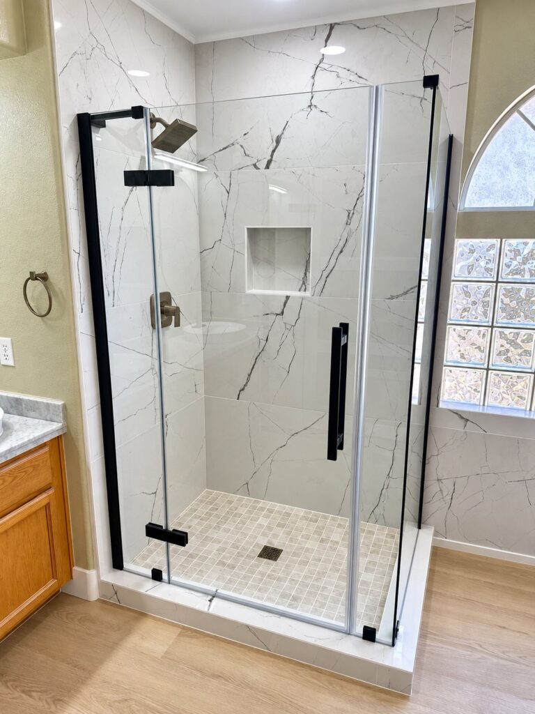 Glass shower enclosure in white marble-look tile with a black frame