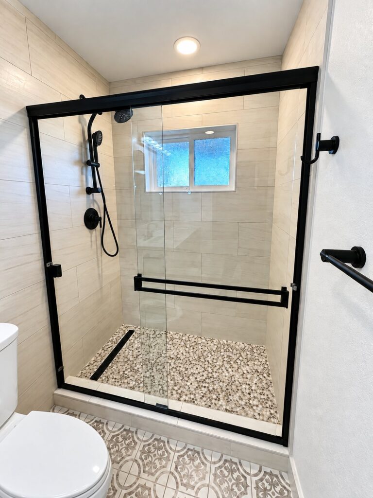 Shower in beige tile with a pebble floor and black-framed sliding door