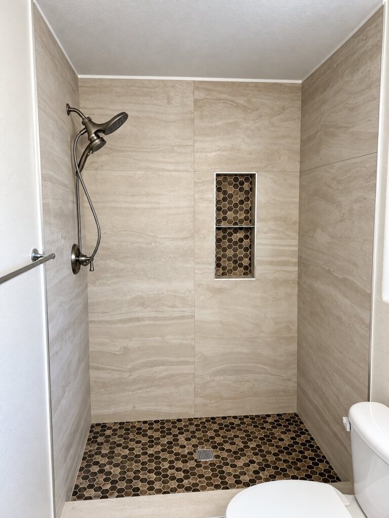 Shower in warm beige tile with a brown hexagon floor and a mosaic niche