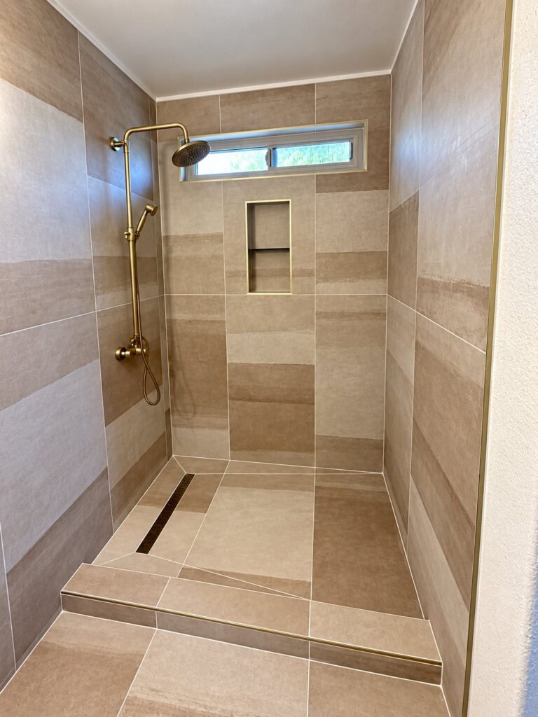 Shower in two-tone beige tile with a linear drain and brushed brass fixtures