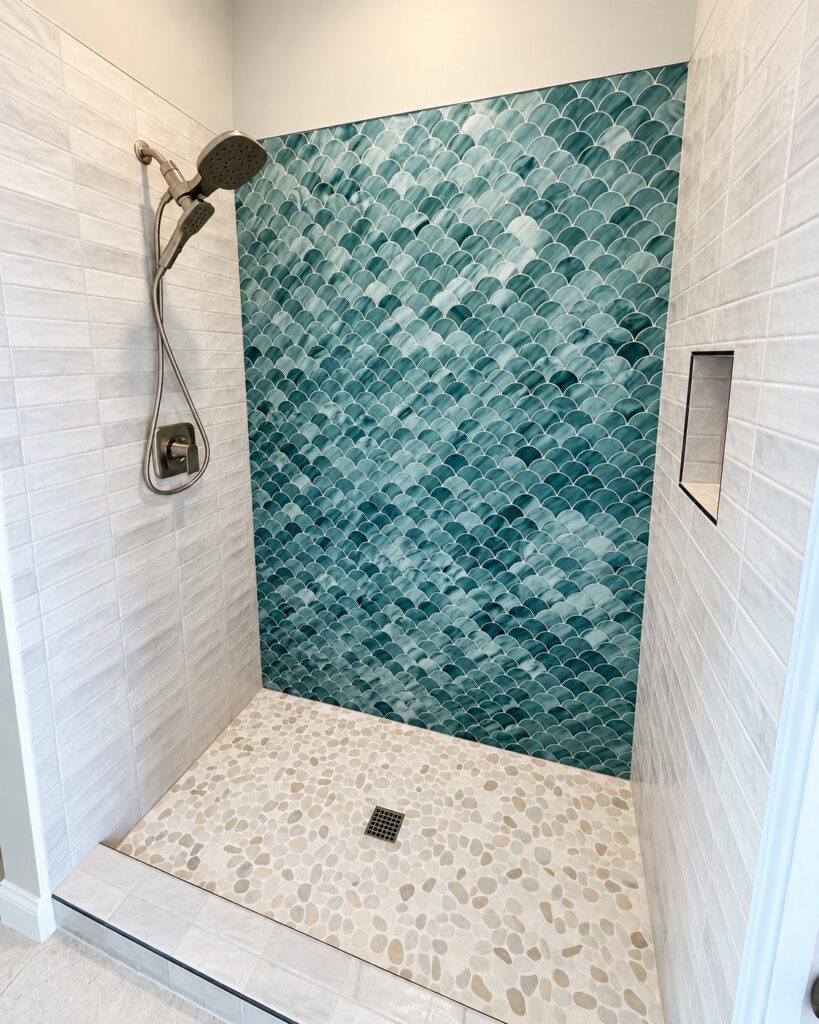 Shower with a teal fish-scale tile wall and a pebble floor