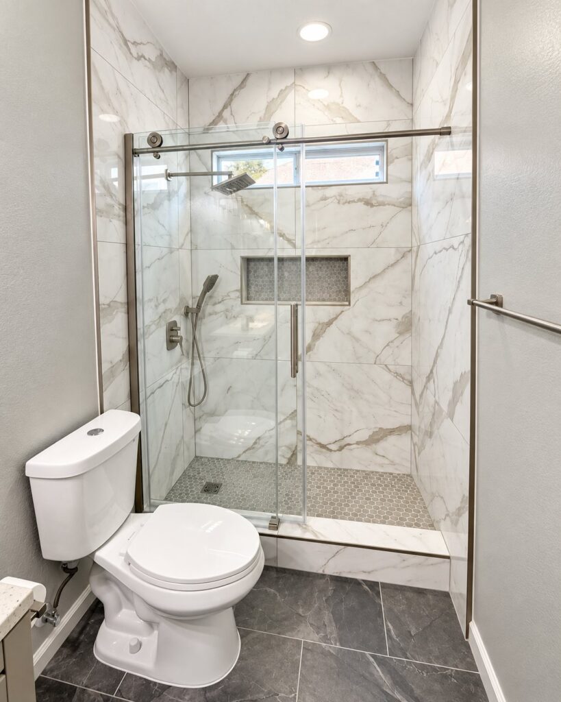 Marble-look tile shower with a sliding glass door and mosaic niche