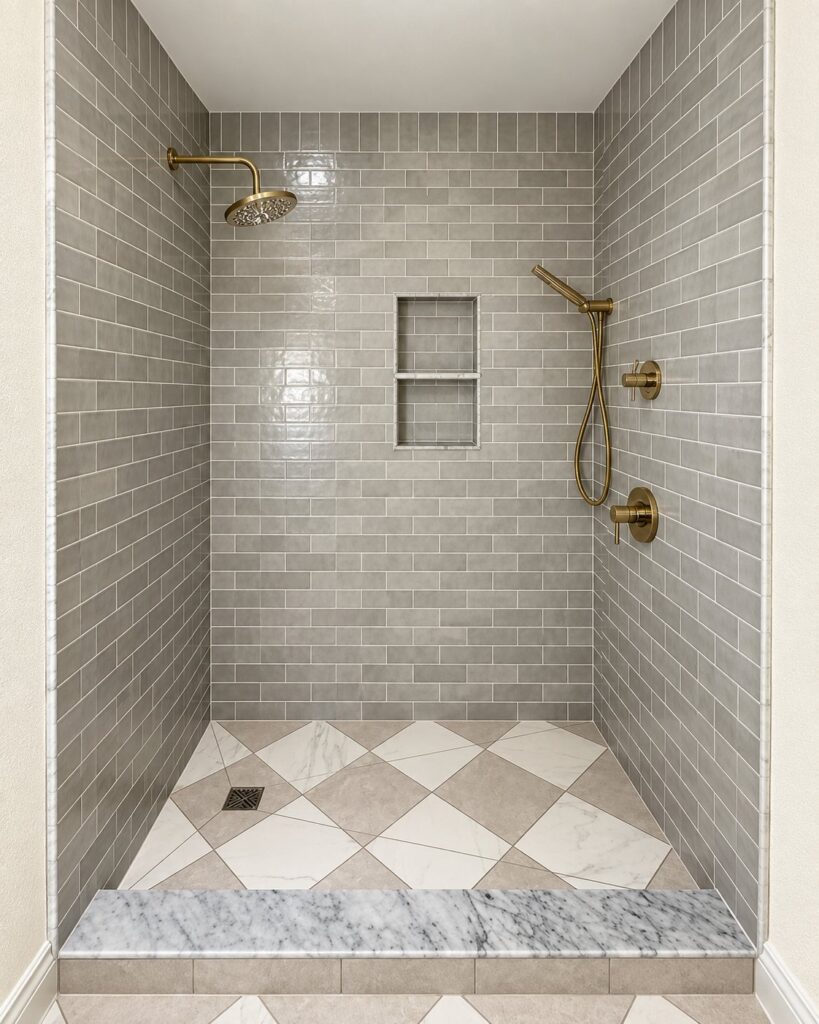 Gray subway tile shower with a diamond-pattern floor and brushed gold fixtures