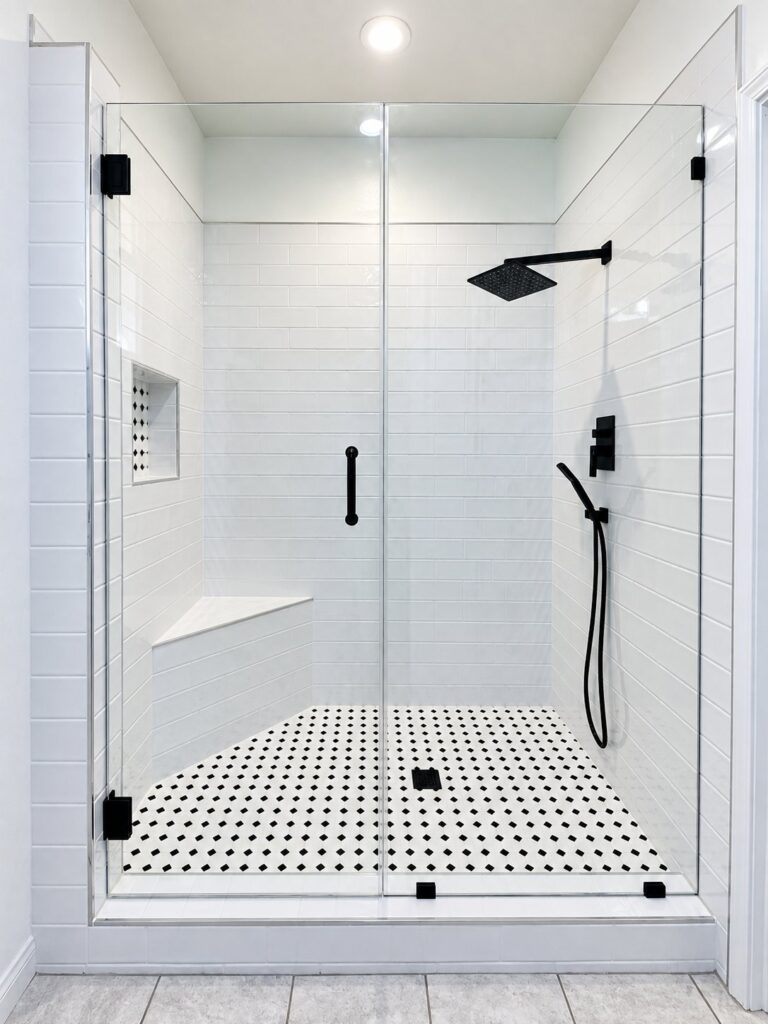 White subway tile shower with a dotted mosaic floor and black fixtures