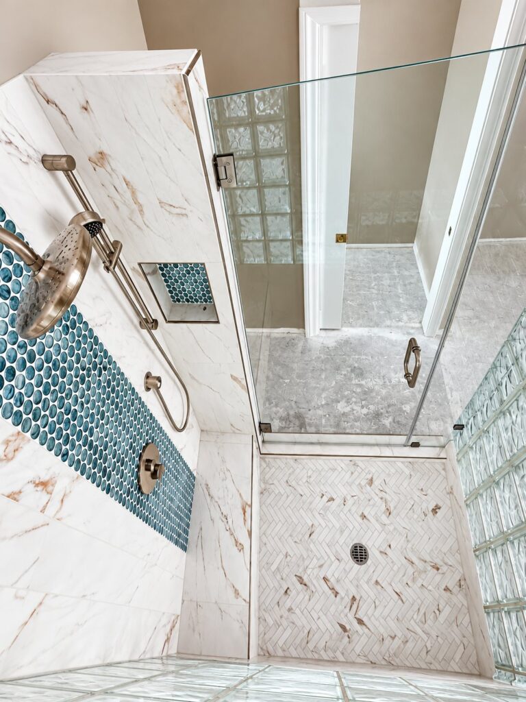 Marble-look shower with a teal penny tile stripe and herringbone floor