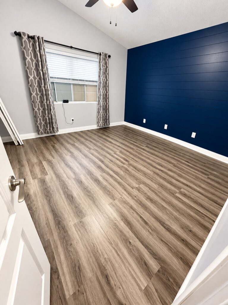 Bedroom with gray plank flooring and a navy shiplap accent wall