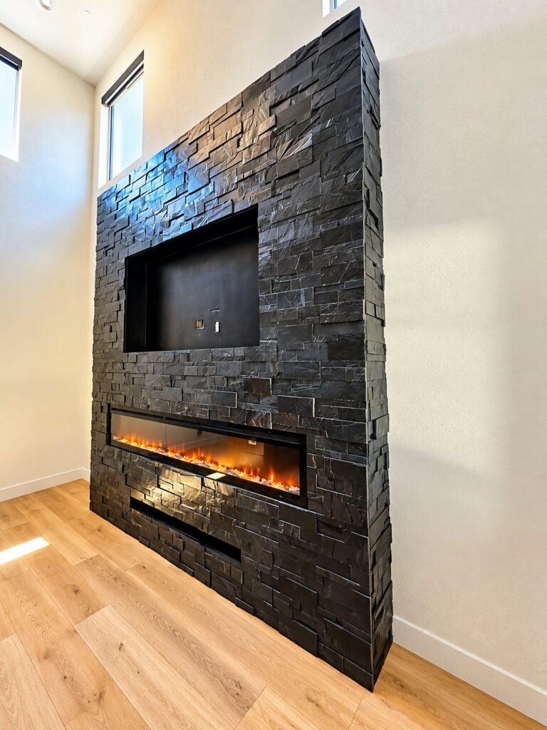 Fireplace wall clad in black stacked stone with a linear fire