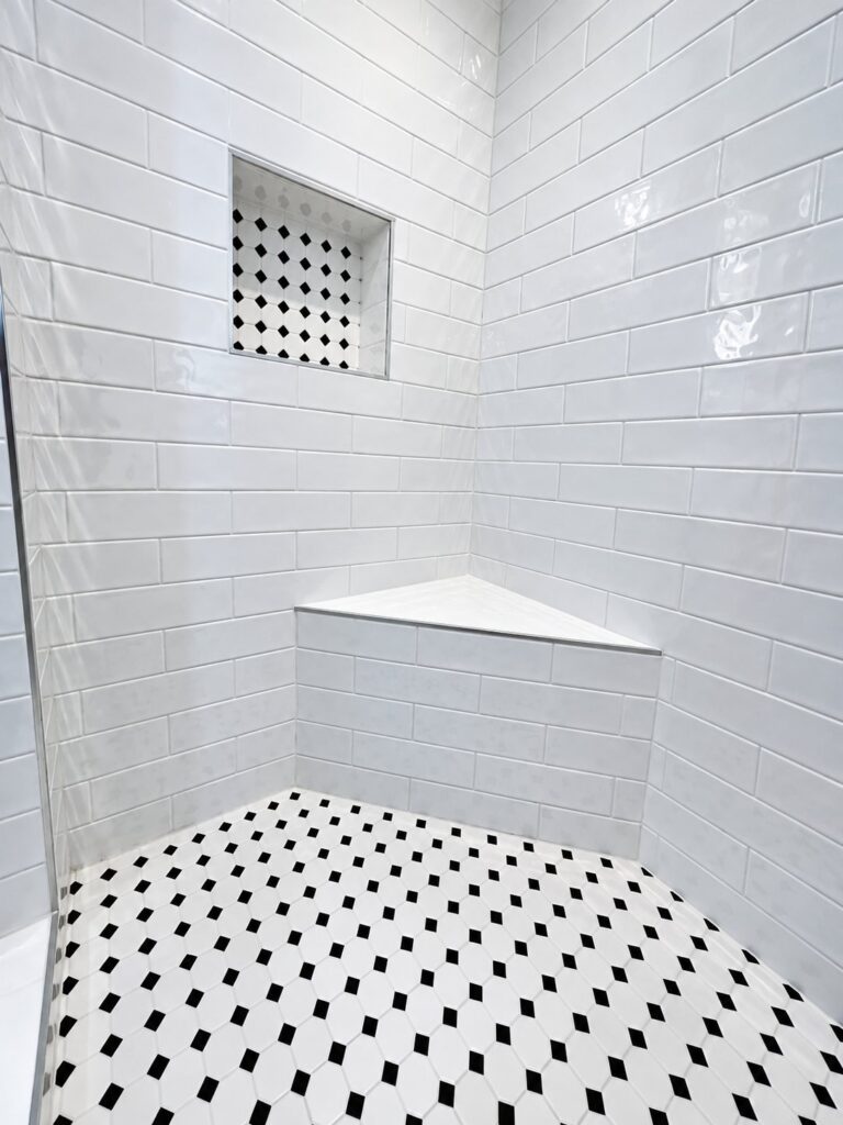 Shower in white subway tile with a bench and a black-and-white mosaic floor
