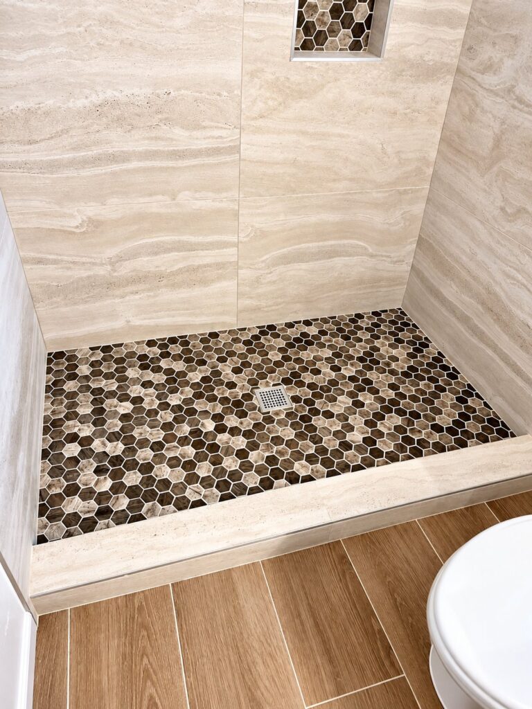 Shower with travertine-look walls and a hexagon pebble floor